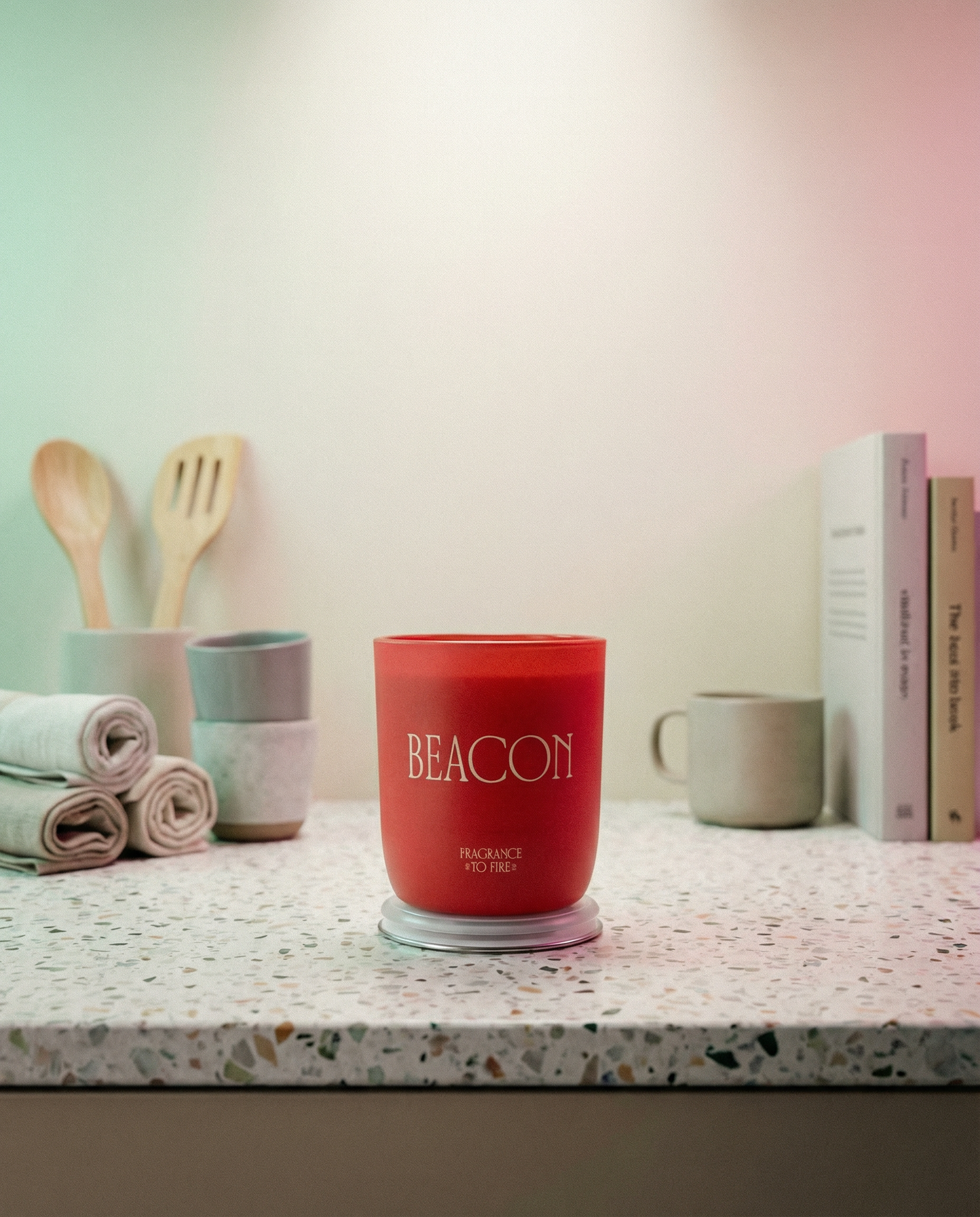 Pink candle labelled 'BEACON' on a kitchen counter with utensils and books in the background.